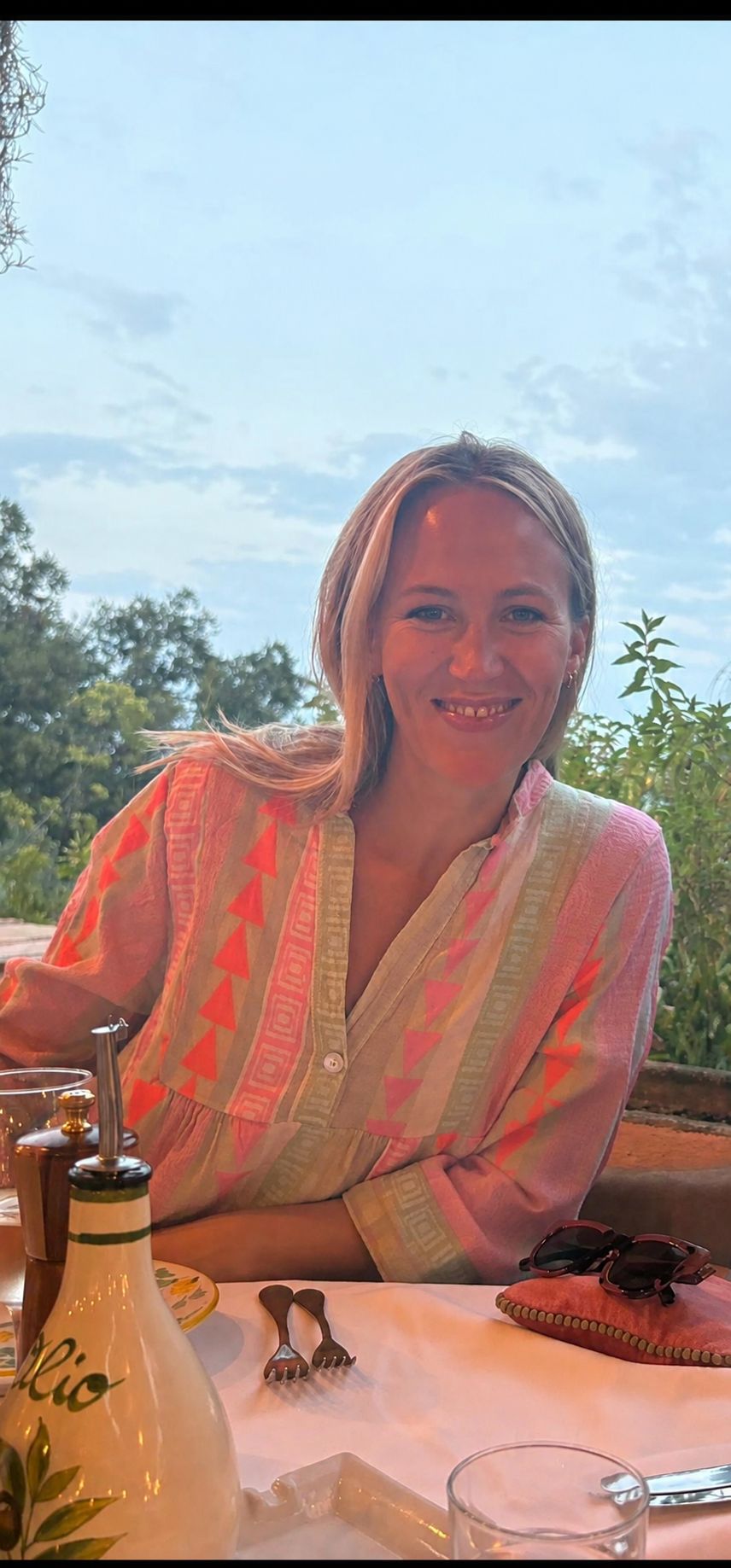 Sarah, founder of The Living Workshop, smiling at an outdoor table in a pink and orange block-print blouse